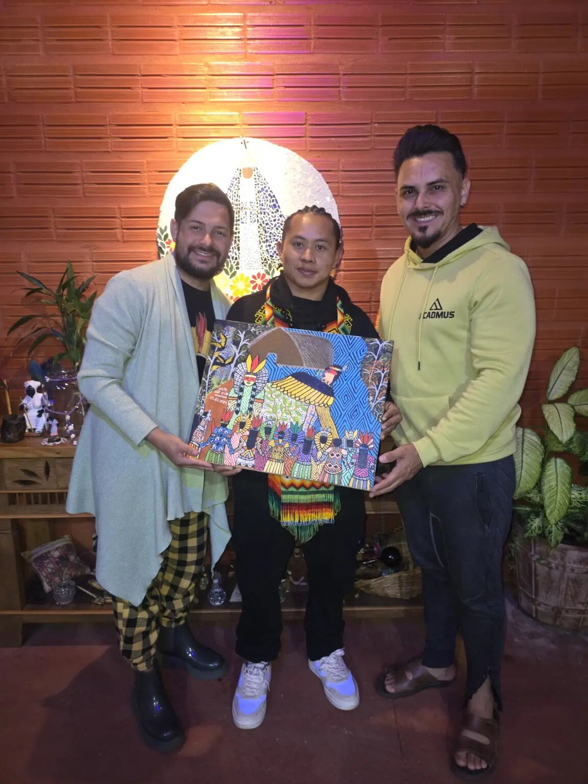 Michael Pereira, Siã Kaia e Bruno Luz segurando obra Huni Kuin de autoria de Siã Kaia no Santuário